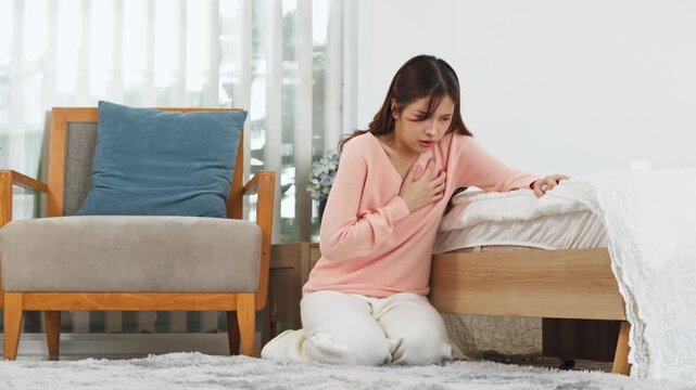 Young Asian woman feeling unwell experiencing sharp chest pain heart attack clutching body alone bedroom looking scared overwhelmed by sudden medical emergency suffering health problem sick stroke