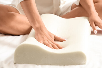 Young woman in pajamas touching soft orthopedic pillow on cozy bed at home, closeup