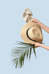 Hands holding sandals with hat and palm branch on blue background