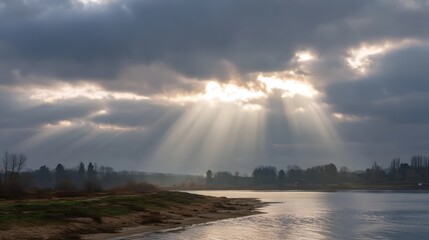 Dramatic sunbeams break through dark clouds over a serene river landscape at dawn