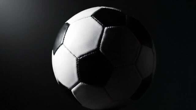 A classic black and white soccer ball illuminated against a dark, dramatic background, highlighting its iconic hexagonal and pentagonal panels.