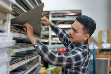 Asian man carpenter inspecting wood boards on storage shelves inside interior furniture material...