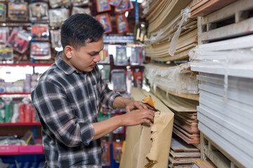 Asian adult man woodworking business owner preparing selected wood boards from shelf and placing...