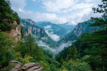 Obraz premium Majestic Mountain Valley Under a Blue Sky with Soft Clouds and Misty Hills Offering a Breathtaking View of Nature's Beauty and Tranquility Surrounding the Scenic Landscape