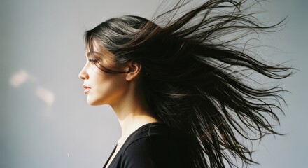 Fototapeta premium Profile of a woman with windblown dark hair against a pale background