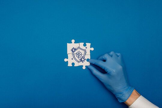 Gloved hand assembling puzzle pieces with a medical shield icon over blue background. Conceptual image for Nipah virus protection, healthcare solutions, immunity, and infectious disease prevention.