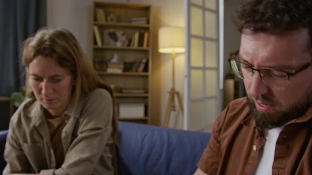 Close up shot of troubled adult man opening envelope getting eviction notice and showing document to wife while sitting on couch together and sorting mail