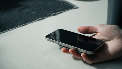 Close-up of a Hand Holding a Smartphone on a Counter with Natural Light （自然光が差し込むカウンターの上でスマートフォンを持つ手のクローズアップ） © takayuki