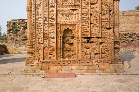 Close-up of intricate arabesque carvings and calligraphic reliefs on a weathered sandstone doorway at the Qutub Minar complex in Delhi. Warm sunlight enhances the rich textures and ornate patterns of
