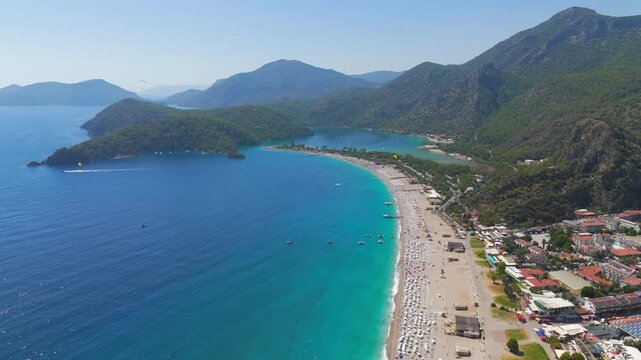 Oludeniz, Turkey. Aerial drone view of multiple paragliders with colorful parachutes flying in distance over Blue Lagoon, Oludeniz Beach and green mountains, summer.. Aerial View
