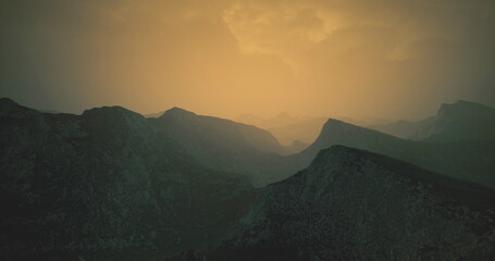 Obraz premium Layers of rugged mountains stretch across the horizon bathed in a warm golden glow. The atmosphere is serene, evoking a sense of peaceful solitude at dusk.