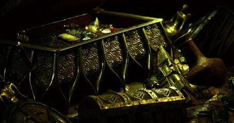 An ornate chest filled with colorful jewels and intricate artifacts rests among various historical objects. The lighting creates a mystical ambiance, enhancing the allure of the treasures. © icetray