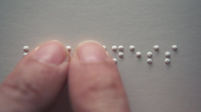 Visually impaired people reading a Braille word "blindness" on paper with their fingers.