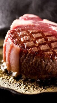 Vertical close-up of a thick premium steak sizzling intensely in golden foaming butter on a hot cast iron pan, showing perfect caramelized sear marks 