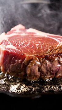 Dramatic close-up of a thick raw ribeye steak sizzling vigorously in hot bubbling fat, producing rising smoke and steam during intense searing on a bl