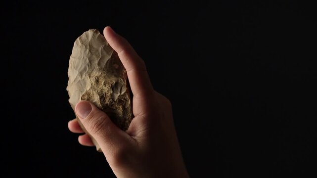 Prehistoric Flint Bifacial Knife from the Sahara Desert Held in Human Hand, Ancient Stone Tool of Early Human Civilization, 4K. Black background. Space for text.