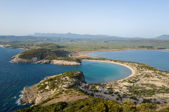 Wide aerial view of Voidokilia Beach's curved sandy shoreline and vivid turquoise bay, bordered by rocky headlands and lush Mediterranean vegetation in Messenia, Peloponnese.