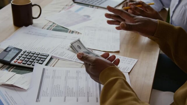 Close up shot of unrecognizable Black man holding cash and managing finances over table with bills and documents, copy space