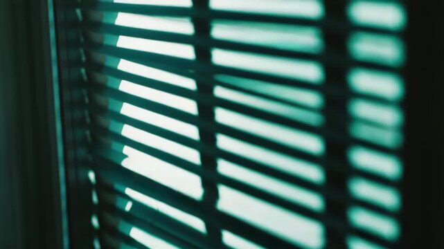 Light filtered through horizontal blinds casts parallel lines and shadows across a wall, creating a minimalist, geometric pattern and a calm, private indoor atmosphere