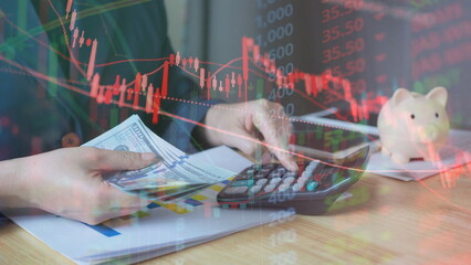 Business person calculating finances with calculator while holding US dollar banknotes, piggy bank and stock market chart overlay. Investment planning, savings, profit, loss  financial risk concept.