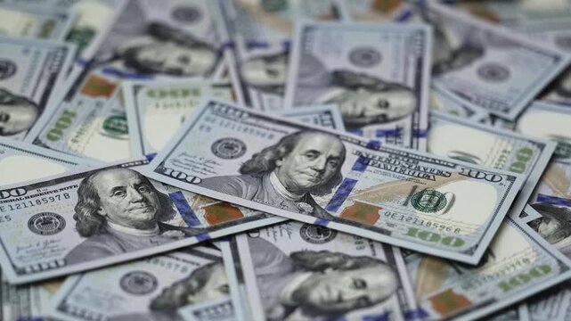 Close-up view of US dollar banknotes stacked in a disordered arrangement, showcasing intricate details and vibrant colors of the currency in a well-lit setting