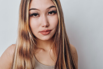 Naklejka premium Young woman with long hair and natural makeup looking at camera with slight smile on neutral background. Portrait closeup with focus on face and eyes in soft lighting and casual style.
