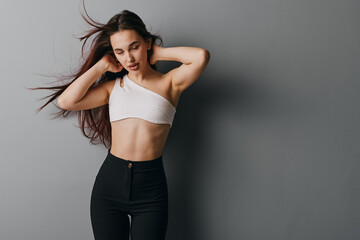 Young woman with long hair wearing white crop top and black high waist pants posing with hands...