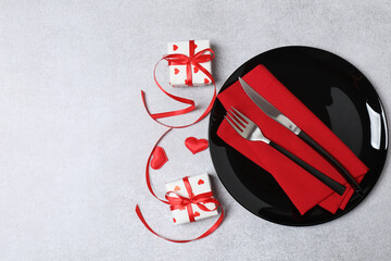 Valentine's Day table setting with plate, fork, knife, gift box and red heart, on tablecloth background top view copy space
