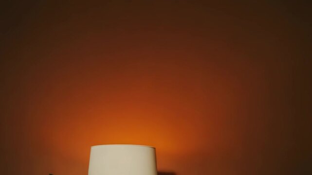Table lamp and small potted green plant on a white table against a peach wall, creating a cozy minimalist interior scene with clean lines and ample copy space for design use