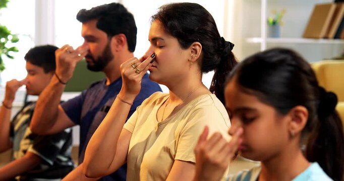Indian young family doing meditation pranayama at home practicing breathing exercise together indoors during peaceful morning hours in a modern lavish living room promoting yoga health wellness