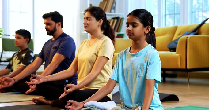Indian young family doing omkar meditation pranayama at home chanting aum breathing yoga together indoors during peaceful morning hours in a modern living room promoting yogic lifestyle