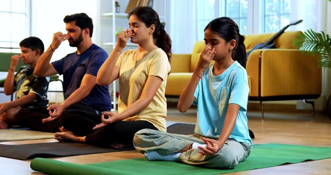 Indian young family doing meditation pranayama at home practicing breathing exercise together indoors during peaceful morning hours in a modern lavish living room promoting yoga health wellness