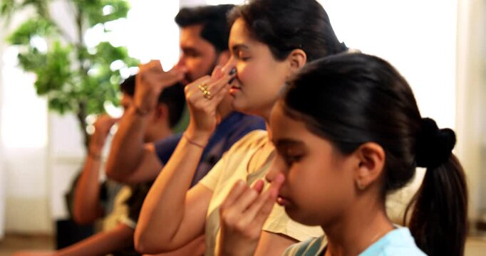 Indian young family doing meditation pranayama at home practicing breathing exercise together indoors during peaceful morning hours in a modern lavish living room promoting yoga health wellness