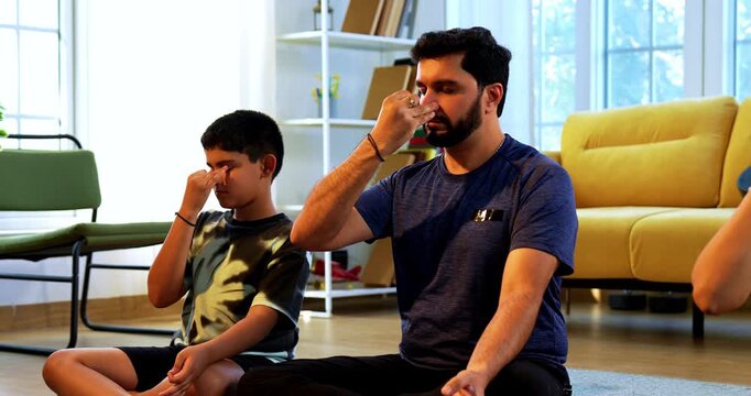 Indian young family doing meditation pranayama at home practicing breathing exercise together indoors during peaceful morning hours in a modern lavish living room promoting yoga health wellness