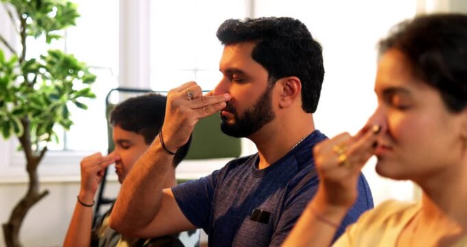 Indian young family doing meditation pranayama at home practicing breathing exercise together indoors during peaceful morning hours in a modern lavish living room promoting yoga health wellness