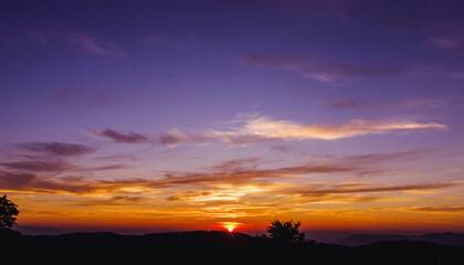 Obraz premium Sunset over a mountain landscape with colorful sky and silhouetted trees.
