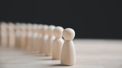 A single wooden figure stands out from a row of identical figures on a wooden table.