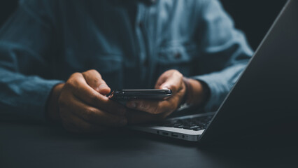 Close-up of hands holding a smartphone, blurred laptop in the background. Dark, moody aesthetic.