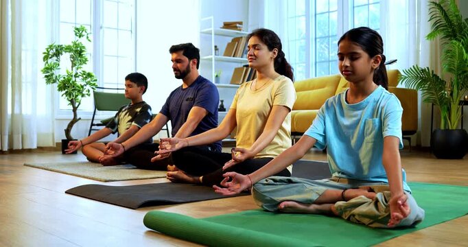 Indian young family doing omkar meditation pranayama at home chanting aum breathing yoga together indoors during peaceful morning hours in a modern living room promoting yogic lifestyle