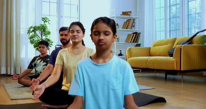Indian young family doing omkar meditation pranayama at home chanting aum breathing yoga together indoors during peaceful morning hours in a modern living room promoting yogic lifestyle