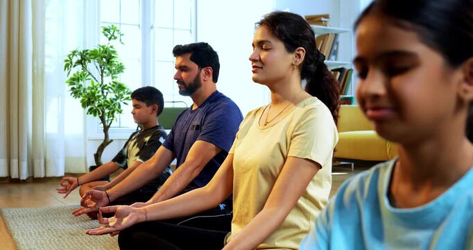Indian young family doing omkar meditation pranayama at home chanting aum breathing yoga together indoors during peaceful morning hours in a modern living room promoting yogic lifestyle