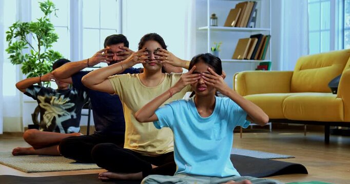 Indian family of four bhramari pranayama or bee breathing exercise practicing yogic breath together indoors during calm morning hours inside a modern home promoting health wellness in yogic style