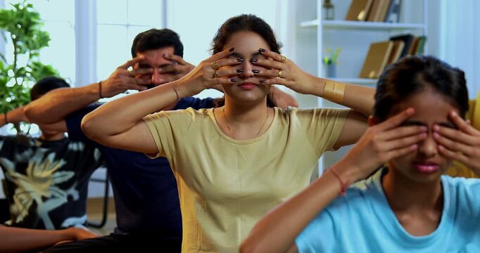 Indian family of four bhramari pranayama or bee breathing exercise practicing yogic breath together indoors during calm morning hours inside a modern home promoting health wellness in yogic style