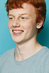 Young man with red hair smiling and looking away in closeup portrait against blue background....