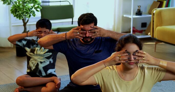 Indian family of four bhramari pranayama or bee breathing exercise practicing yogic breath together indoors during calm morning hours inside a modern home promoting health wellness in yogic style