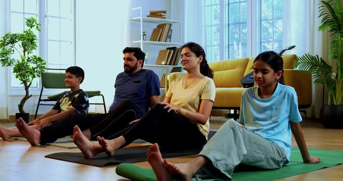 Indian family doing yog asana at home practicing ardha matsyendrasana seated spinal twist yoga together indoors during calm morning hours inside a modern lavish living space promoting health