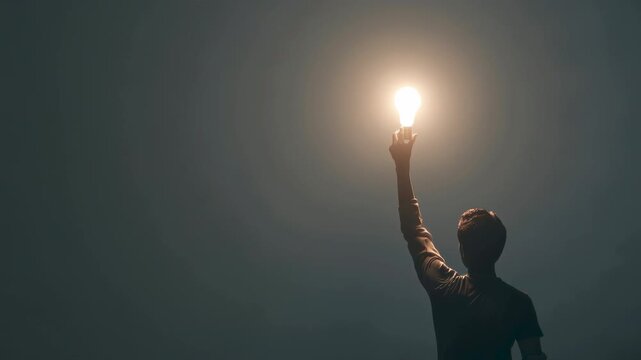 Idea and inspiration from a lightbulb in a hand. This success vision creativity and motivation concept shows a silhouette raising a bright light towards a dark sky for a professional goal.