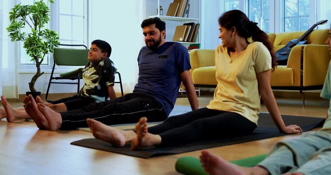 Indian family doing yog asana at home relaxing legs between yoga session while sitting on floor together indoors during calm morning hours in modern lavish living space promoting healthy lifestyle