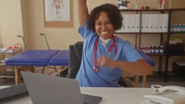 Woman nurse smiling raising arm over laptop on desk in clinic building; medical teamwork joy empowerment.