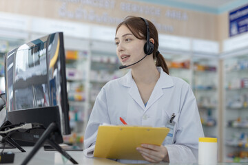 Female pharmacist wearing headset using computer to consult patients online. Healthcare...